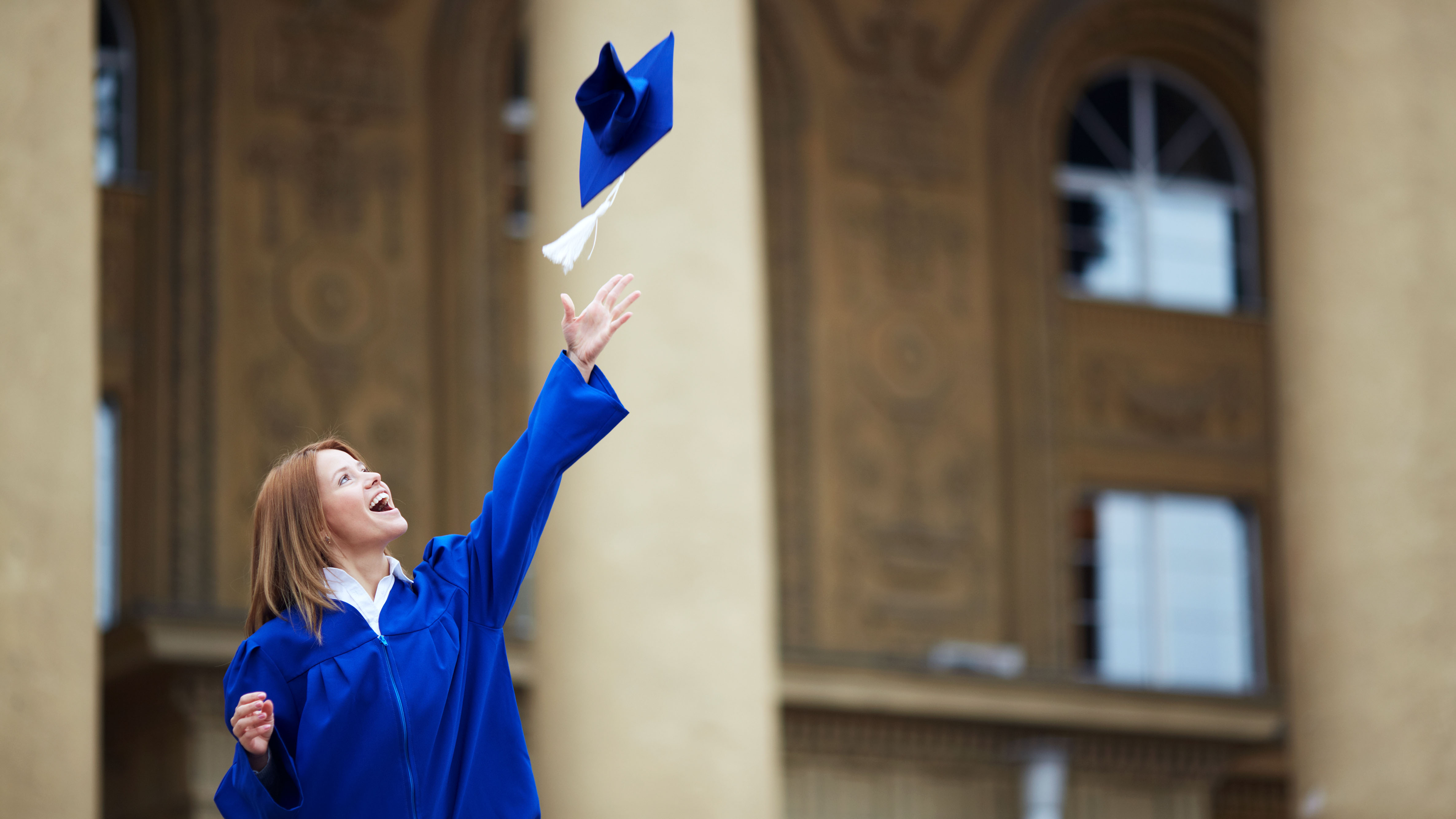 Graduate in graduation gown through cap in the air and smiling