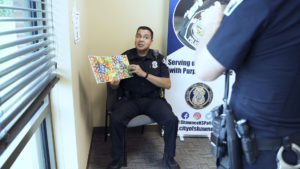 Officer Madrigal reading from Eric Carle's The Very Hungry Caterpillar. An officer in the foreground films with his iPhone for livestream