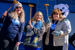 Mary Shea, CEO; Lindsey Moore, CXO; and Allison Schultz, Business Development Officer holding toilet plungers given as an award for fundraising with Polar Plunge